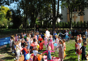 wszystkie dzieci tańczą w grupowych kołach, trzymając balony i śpiewają piosenkę